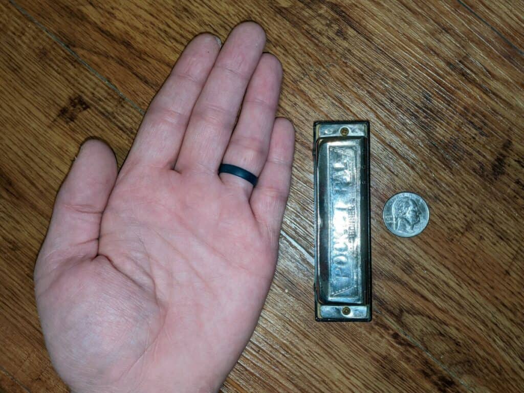 my hand next to a harmonica and a quarter for scale