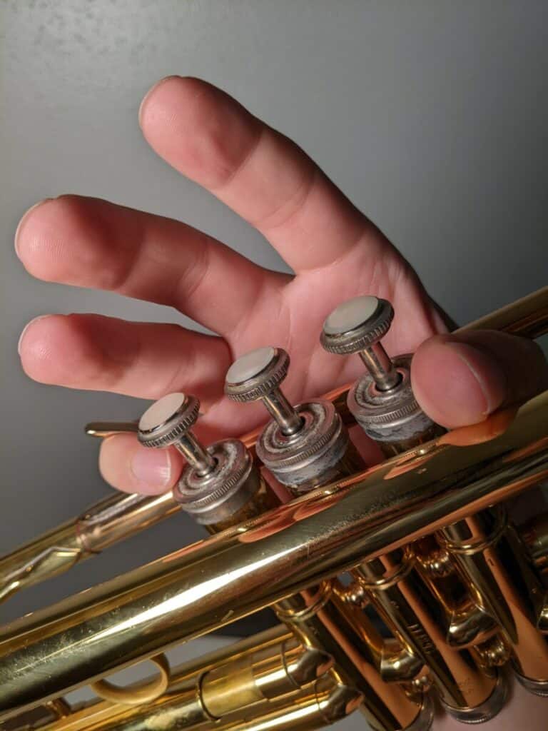 right hand holding the trumpet with the thumb between the two bores and the right pinky in the hook