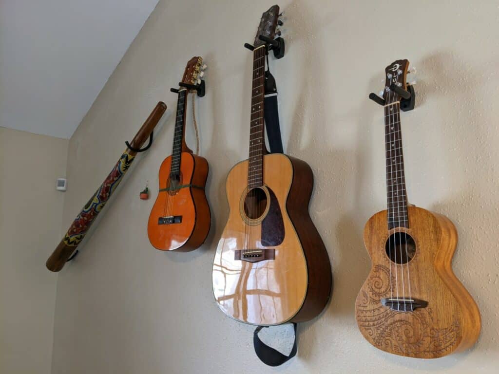 two guitars and a didgeridoo and a ukulele hanging on the wall.